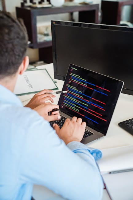 A close-up image shows an open laptop on a wooden surface displaying lines of green and white code on a dark background, suggesting programming or technical work. Beside the laptop, there is a coffee